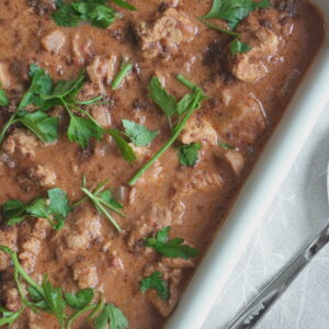 Coconut Butter Chicken (Murgh Makhani) garnished with fresh coriander leaves with garam masala powder in a white casserole dish with a karge serving spoon on the side