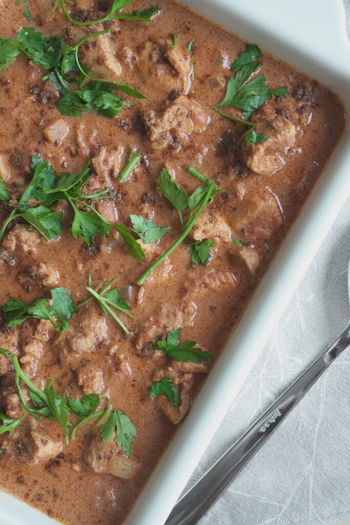 Coconut Butter Chicken (Murgh Makhani) garnished with fresh coriander leaves with garam masala powder in a white casserole dish with a karge serving spoon on the side