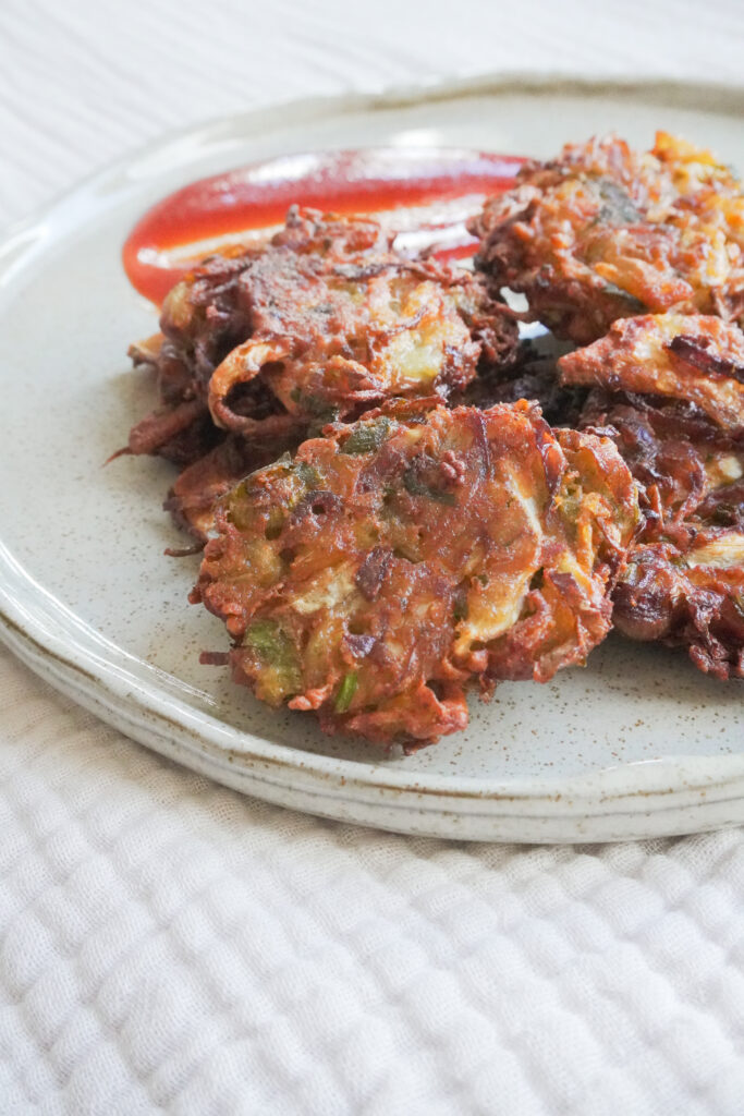 A plate of Vegetable Pakoras with sauce on the side on a gray beige plate