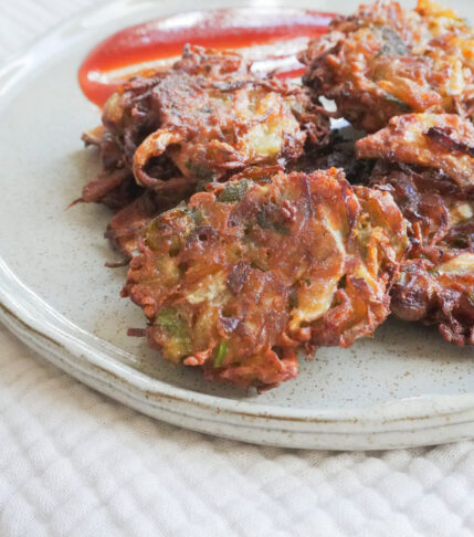 A plate of Vegetable Pakoras with sauce on the side on a gray beige plate