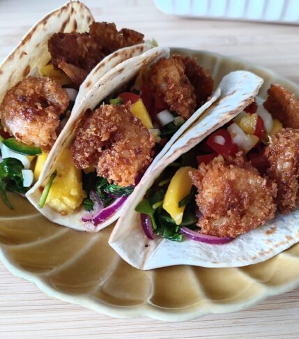 Crispy Shrimp Tacos with Spicy Mango Salsa on a scallop patterned ochre plate on a working surface