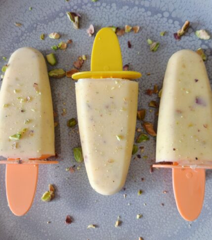Mango Cardamom Pistachio Popsicles topped with roasted pistachios on a large gray plate