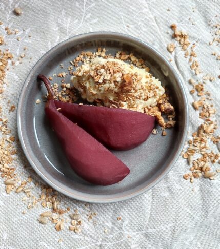 Stoofpeertjes : Two pieces of pear with a scoop of ice cream and a sprinkle of granola on a dessert plate surrounded by a ring of granola trail