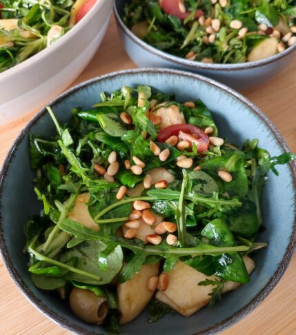 The Everything Salad portioned between two blue bowls with the large bowl of leftover salad in the background on a working surface