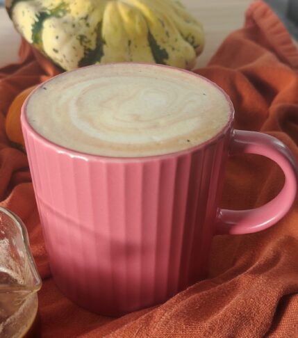 accompanied by a shot of espresso in a shot glass with a stainless steel mug and pumpkins on terracotta coloured fabric