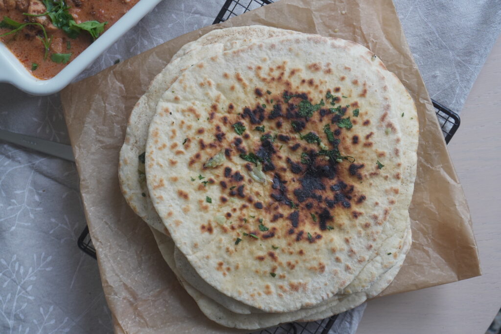 Garlic Cilantro Naan on brown parchment paper and a white casserole dish with butter chicken in it