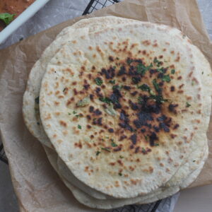 Garlic Cilantro Naan on brown parchment paper and a white casserole dish with butter chicken in it