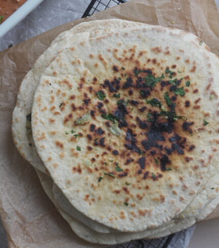Garlic Cilantro Naan on brown parchment paper and a white casserole dish with butter chicken in it