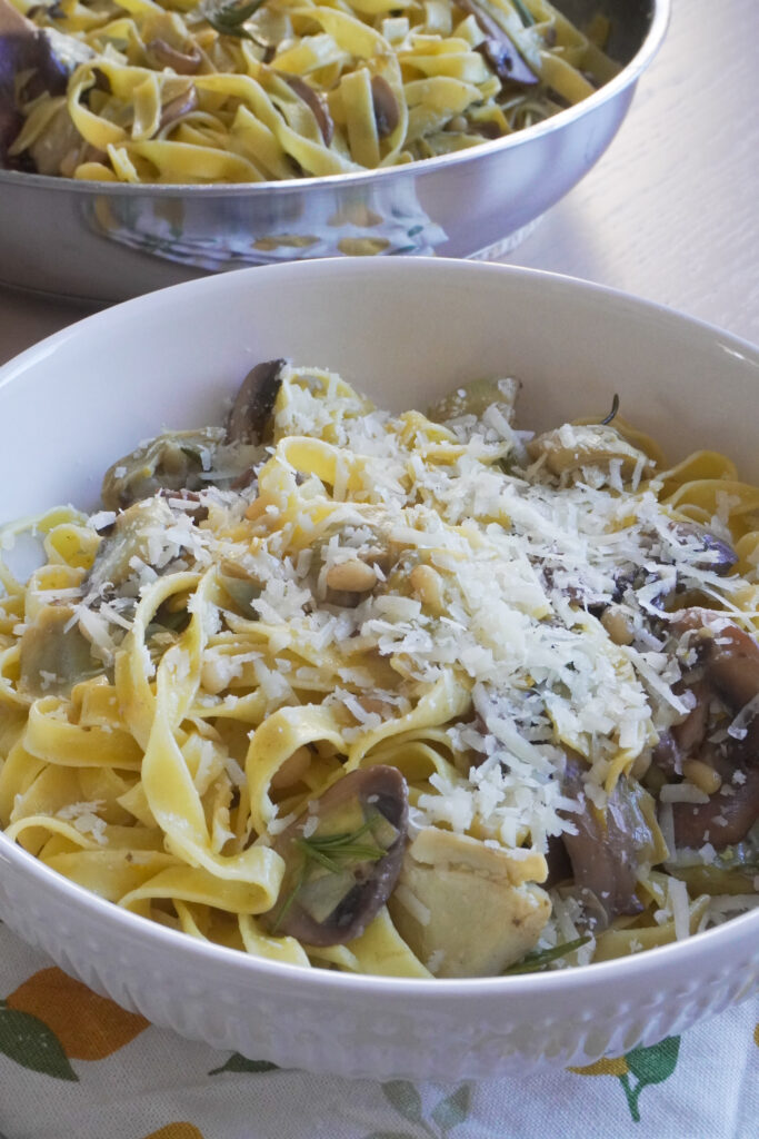 B roll 1 : One Pan Lemon Butter Tagliatelle with Mushrooms & Artichokes in a large white bowl on a tea towel with lemon prints and the pan filled with the remaining pasta on the side