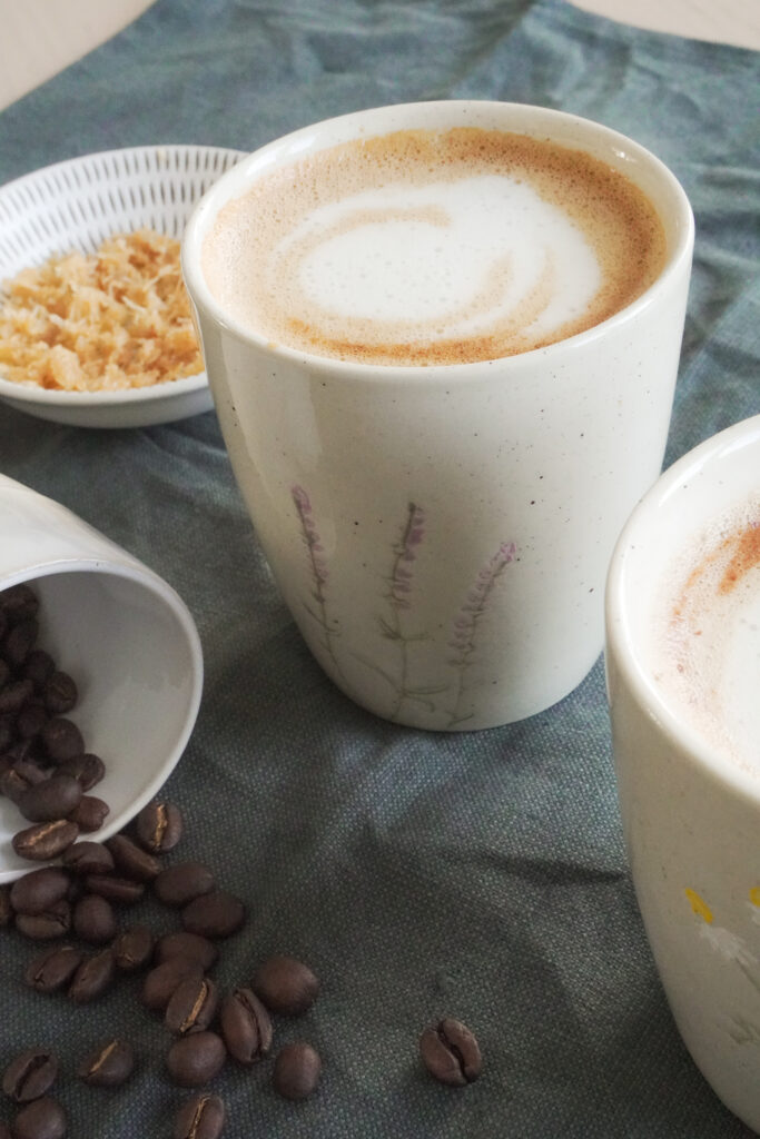 B roll 1: Dubai Chocolate Inspired Mocha in two cups with some coffee beans on the side and crunchy knafeh topping on the side on a dark green fabric from a side shot closeup