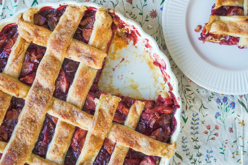 A closeup of the Apple Cherry Almond Pie with a slice missing and the missing slice is on a white plate opposite it