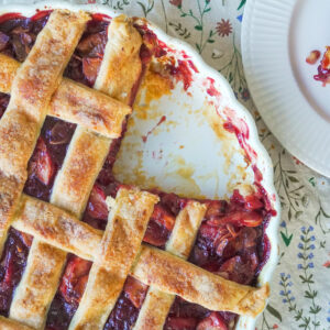 A closeup of the Apple Cherry Almond Pie with a slice missing and the missing slice is on a white plate opposite it
