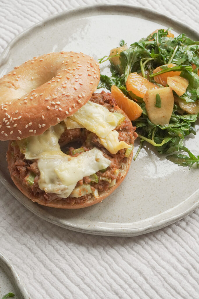 B roll 2: Side view of Airfryer Tuna Bagel Melt with a side of wild peach and mandarin arugula salad on modern ceramic plate on textured beige table cloth
