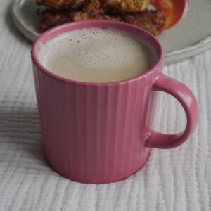 Chai Masala Latte in a pink cup with a plate of Pakoras on a beige grey plate in the background