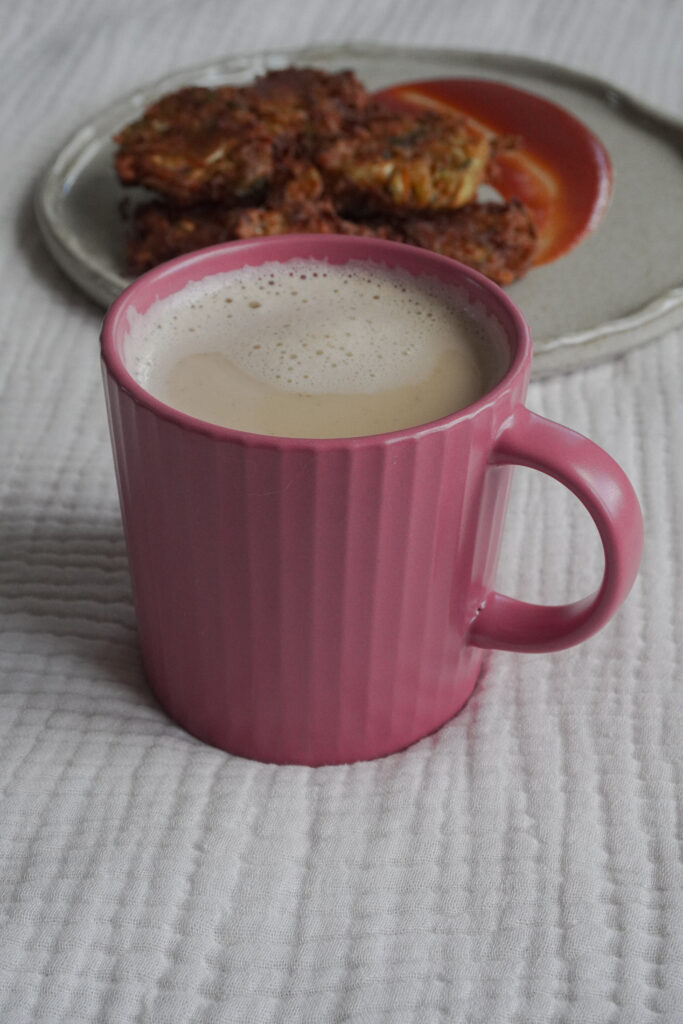 Chai Masala Latte in a pink cup with a plate of Pakoras on a beige grey plate in the background