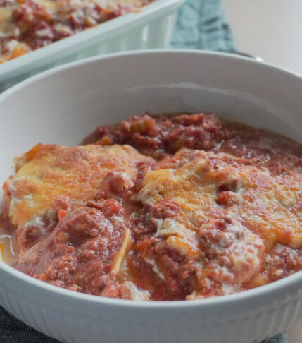 A serving of Deconstructed Lasagna in a white bowl with the rest in a casserole dish in the background
