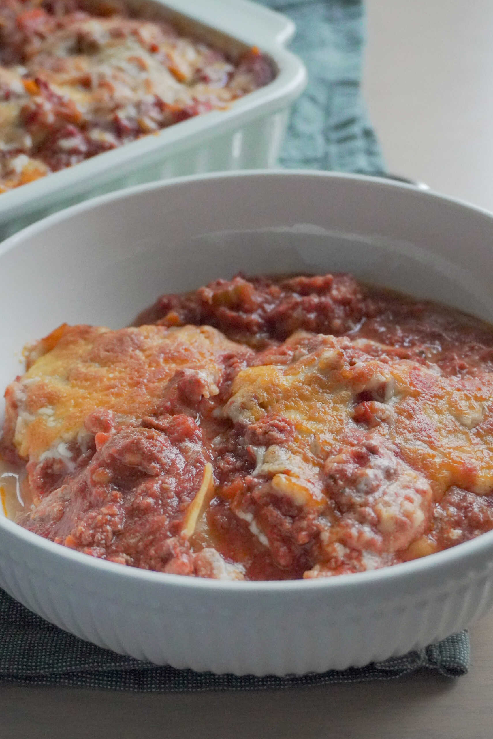 A serving of Deconstructed Lasagna in a white bowl with the rest in a casserole dish in the background