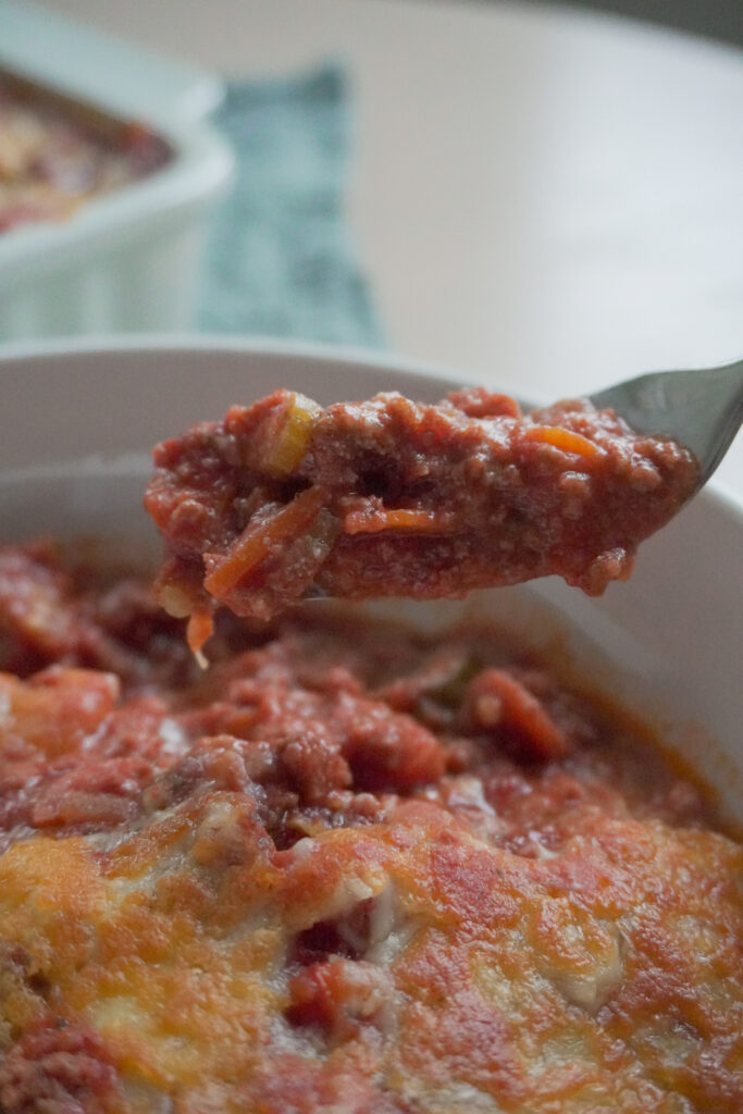 A forkful of Deconstructed Lasagna in a white bowl with the rest in a casserole dish that can be seen in the background
