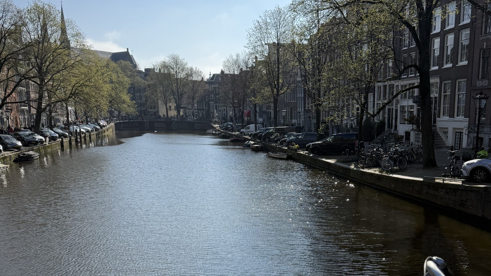 Sunlight sparkling on a canal with trees and bicycles on a bridge