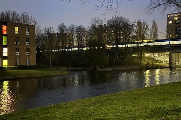 A peaceful evening view of a river with green grass and city lights reflecting on the water